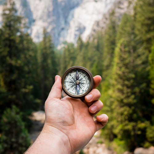 Hand holding a compass in front of hiking path with nice view